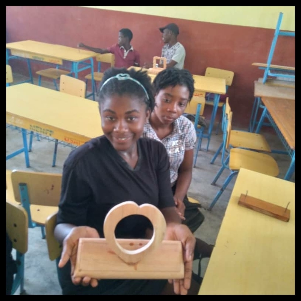 Two women sitting at a table holding up a wooden object.