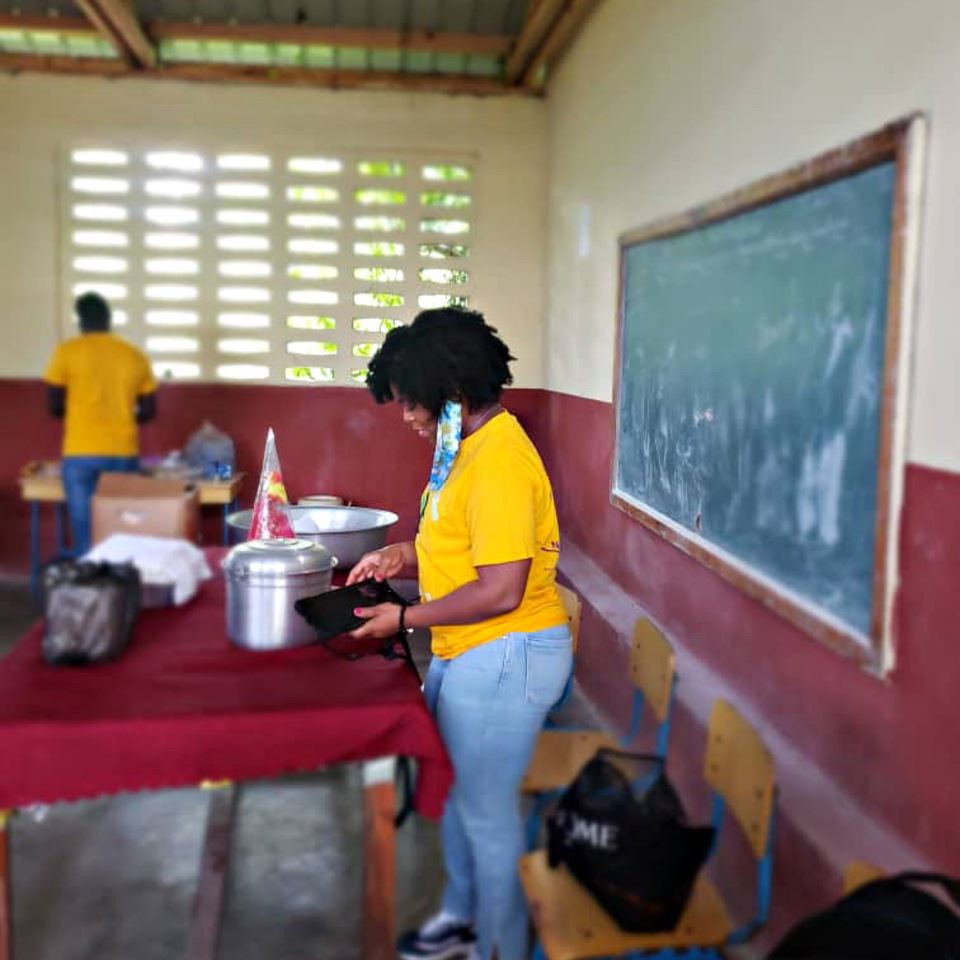 A woman in yellow shirt standing next to table.