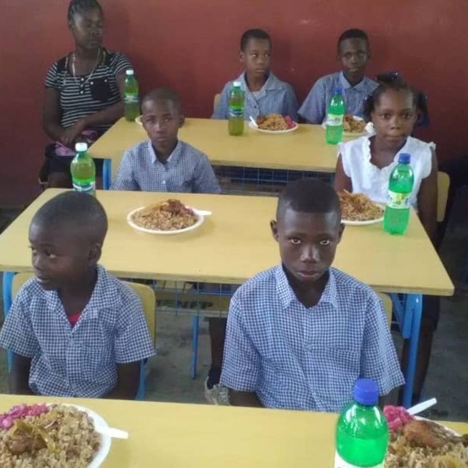 A group of children sitting at tables eating food.