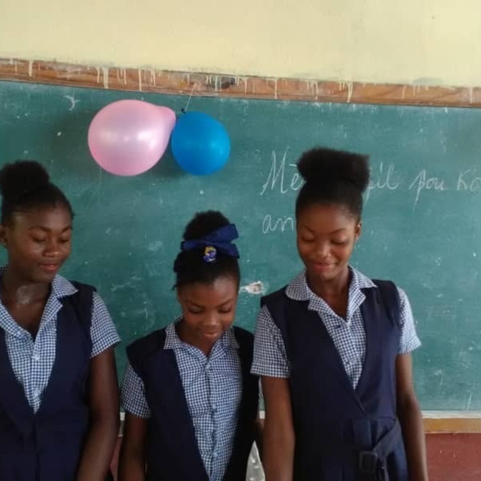 Three girls in school uniforms standing next to a chalkboard.