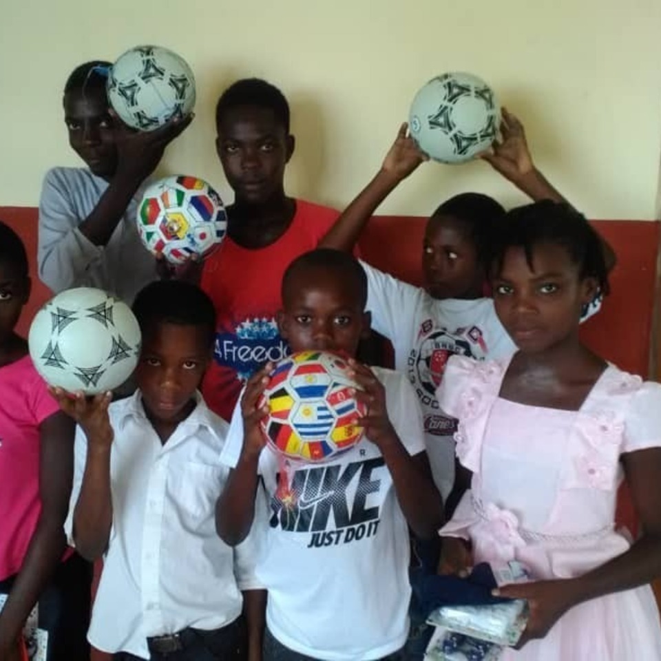 A group of children holding soccer balls in front of their faces.