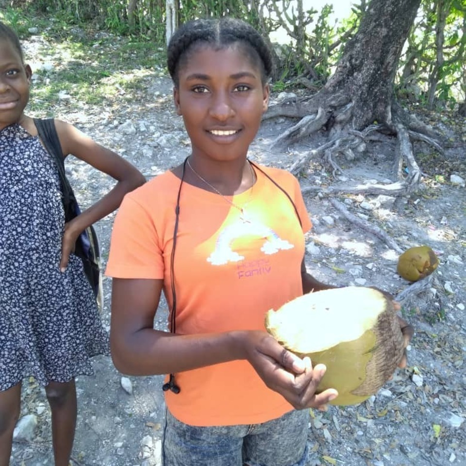 A girl holding a coconut and smiling for the camera.