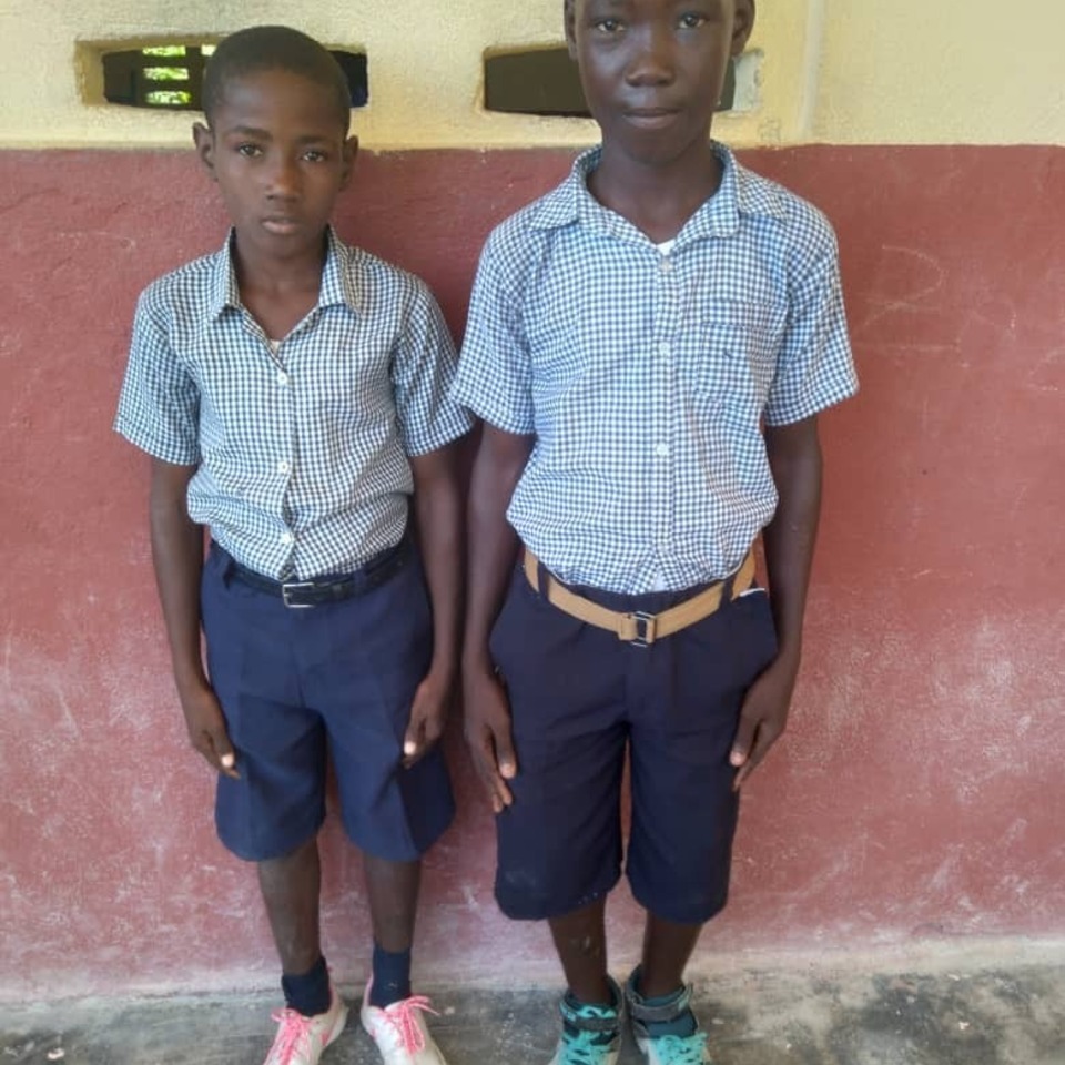 Two boys standing next to each other in front of a wall.