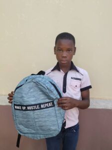 A boy holding a backpack in front of a wall.