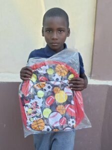 A young boy holding up a bag of sports equipment.