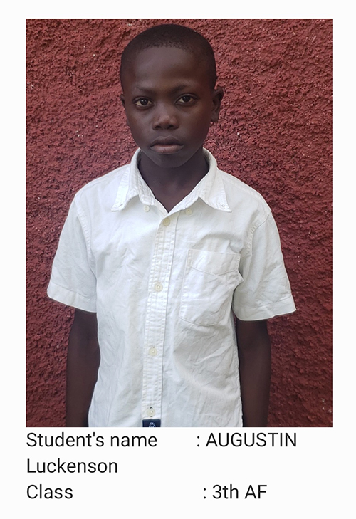 A young boy in white shirt standing next to red wall.