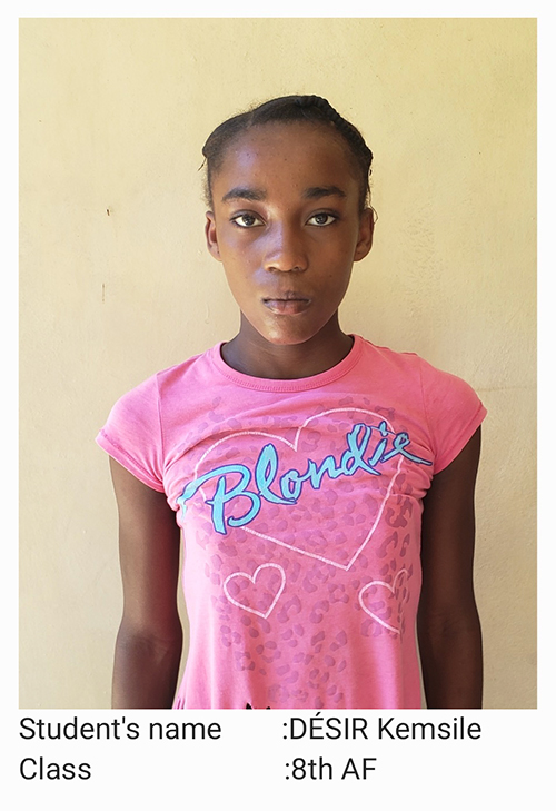 A young girl in pink shirt standing next to wall.