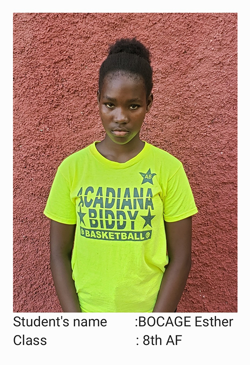 A young girl wearing a yellow shirt standing in front of a wall.