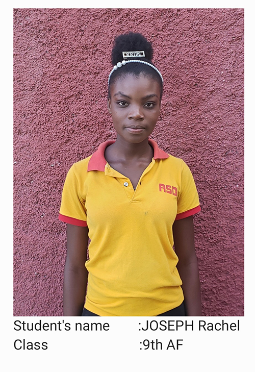 A young woman in yellow shirt standing next to pink wall.