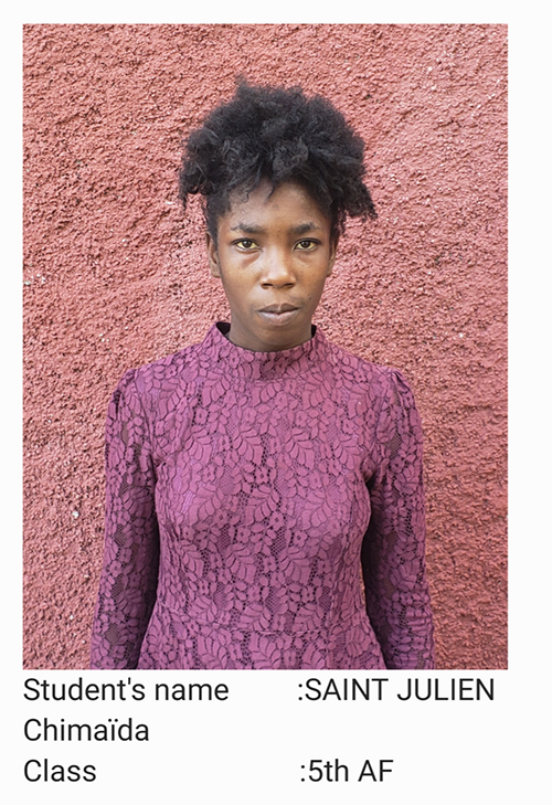 A woman in purple shirt standing next to pink wall.