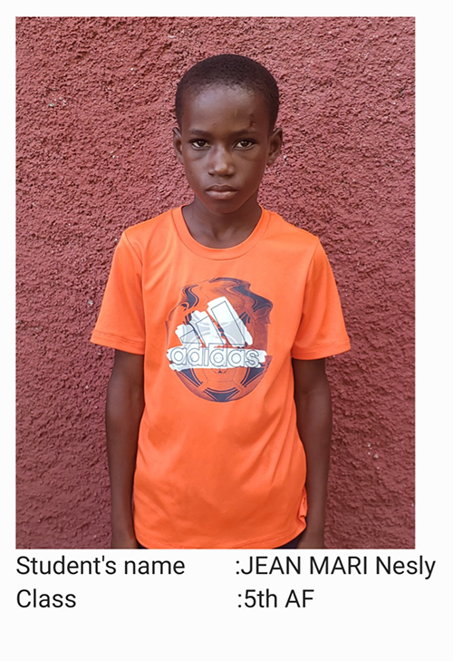 A young boy wearing an orange shirt standing in front of a wall.