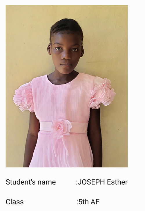 A young girl in pink dress standing against wall.