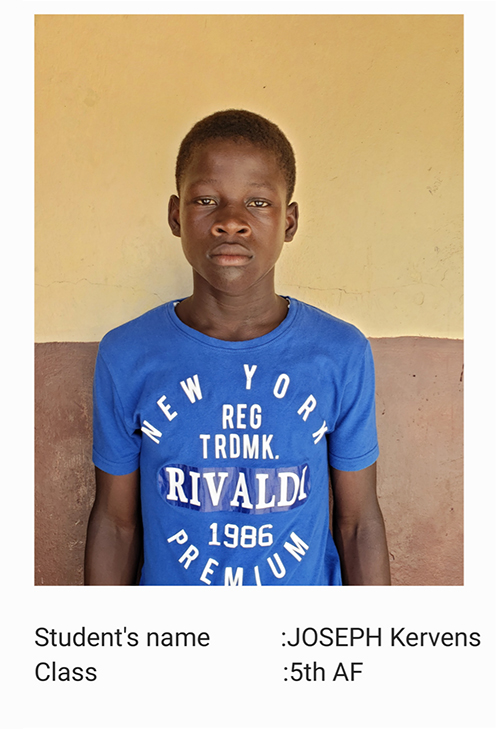 A young boy wearing a blue shirt and standing in front of a wall.